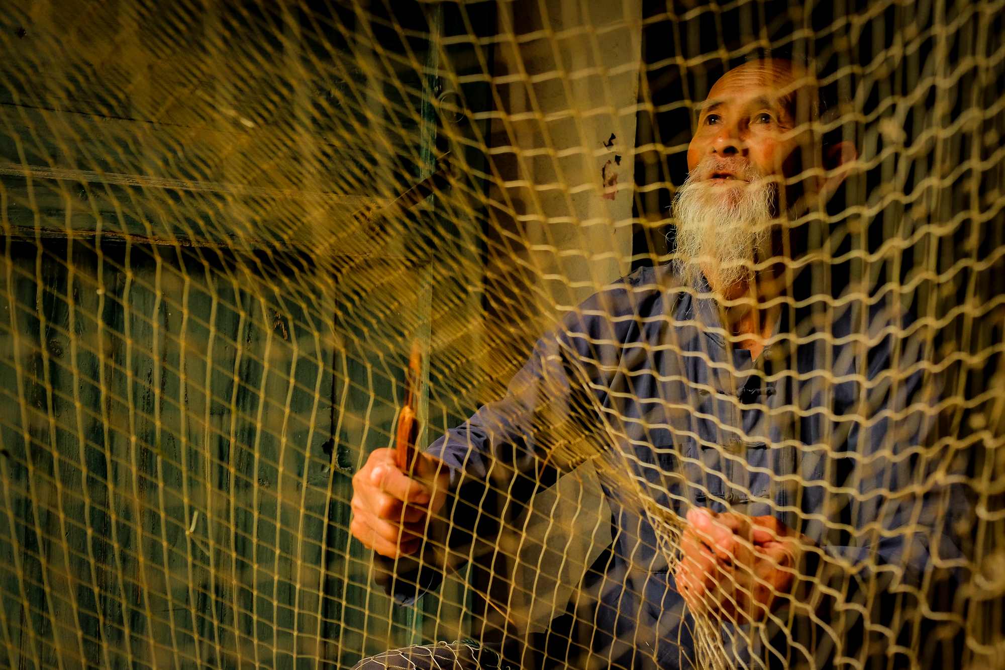 A fisherman fixing his fishing net in his house at the fishing village in Yangshuo, China
